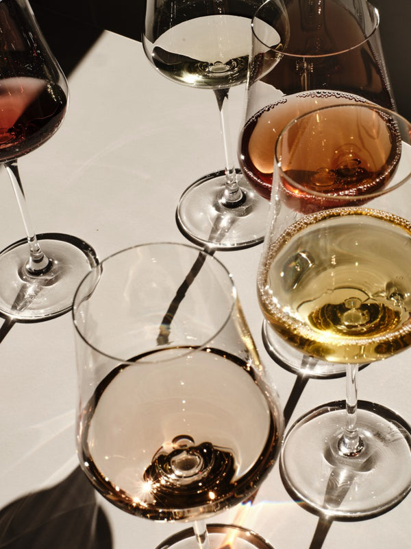 Multiple wine glasses filled with different types of wine on a white surface